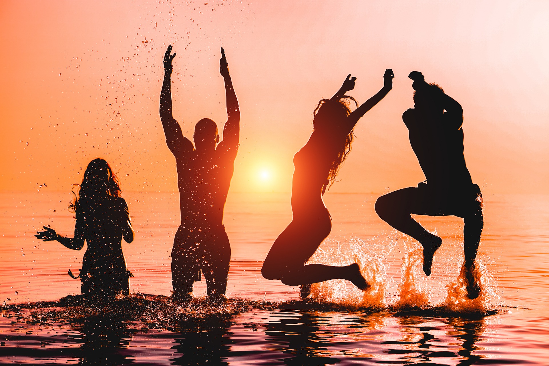 Happy friends jumping inside water on tropical beach at sunset - Ibiza