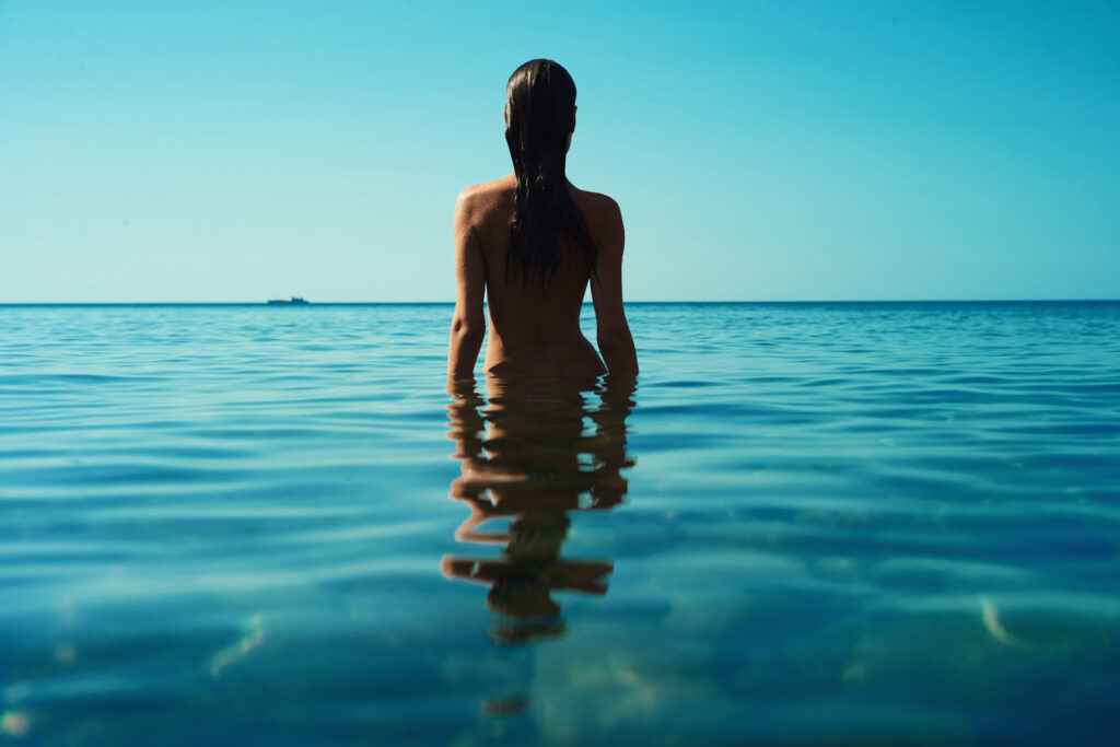 Junge Frau genießt die Sonne am FKK-Strand von Ibiza – entspannter Moment am Meer