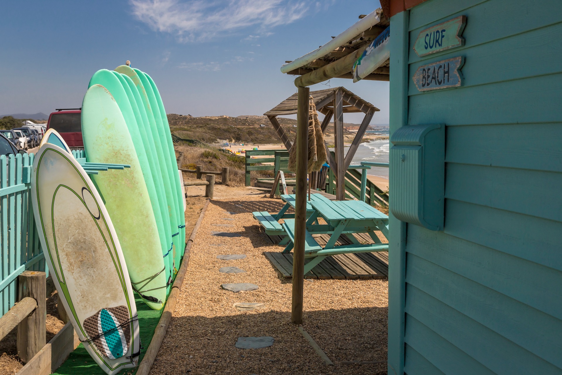 Unas tablas verdes de surf descansan sobre una valla en una play FKK-Lifestyle