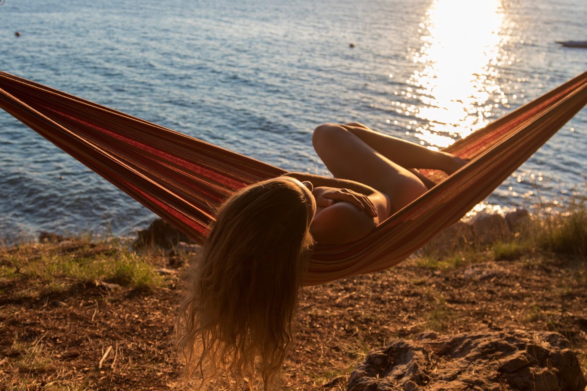 Naked girl on a hamock during sunset, nudist camp Konobe on Krk Topless young woman covering her breasts by hands