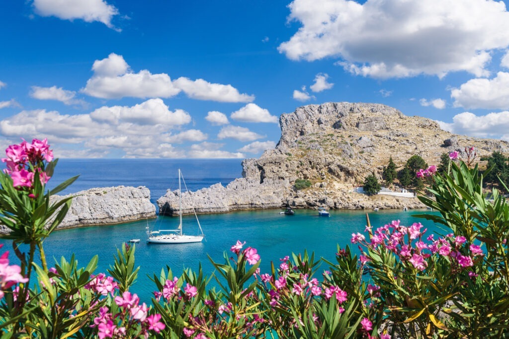 Blick auf die St. Paul’s Bay auf Rhodos mit Segelboot, türkisblauem Wasser und felsiger Küste