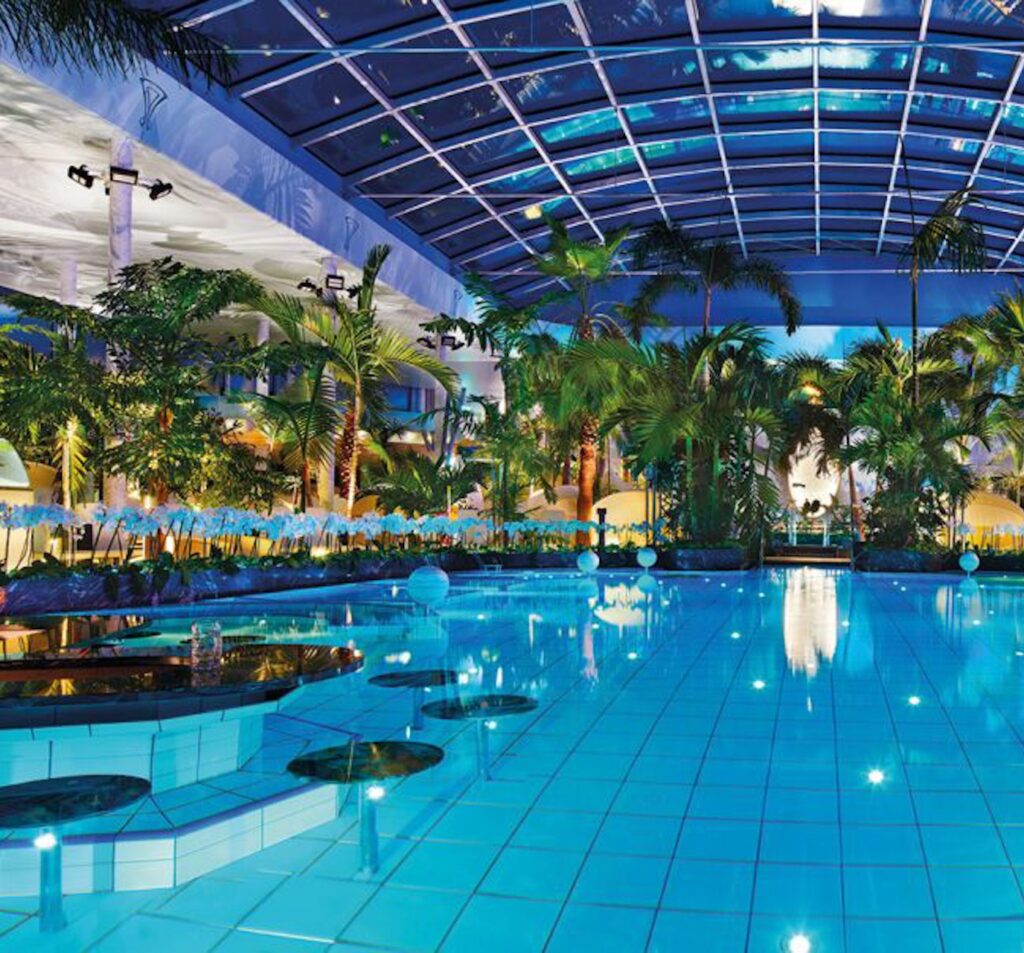 FKK-Resort Desire Riviera Maya mit Palmen, Gartenwegen und Strohdach-Pavillons in der Sonne.