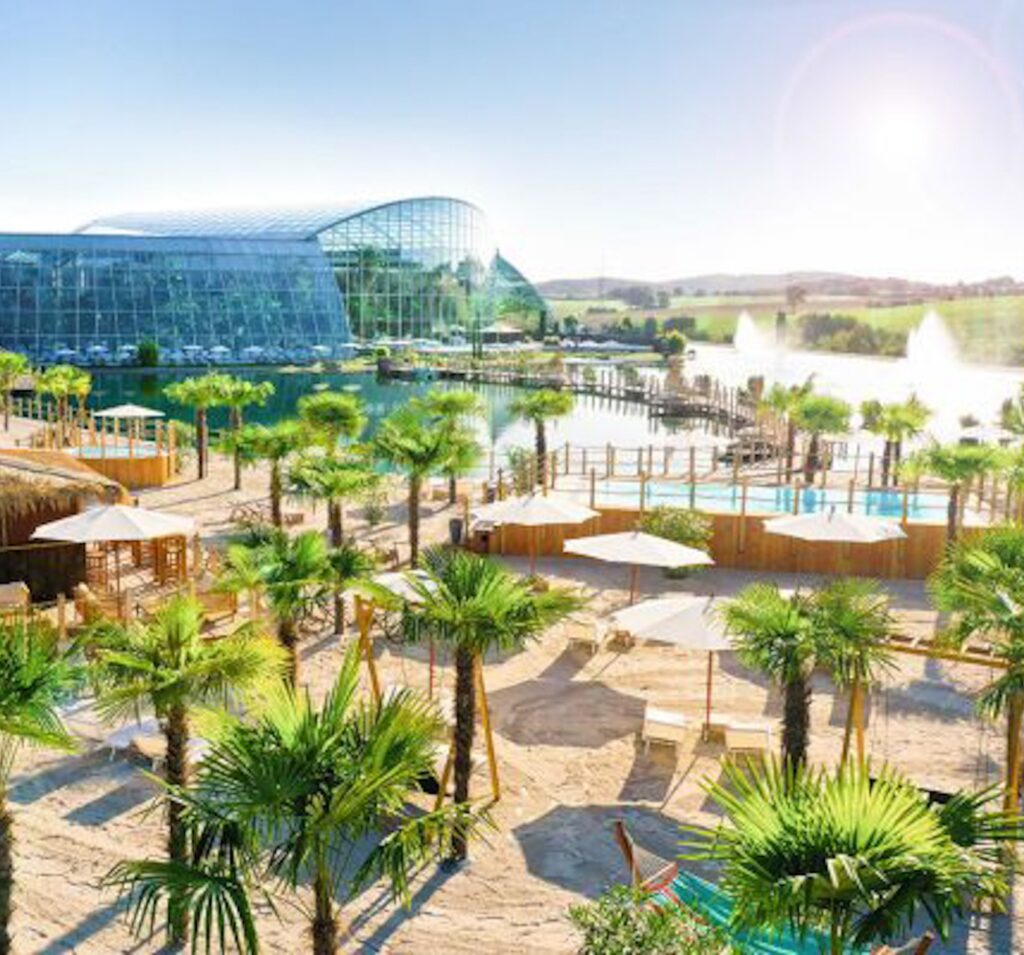 FKK-Resort Desire Riviera Maya mit Palmen, Gartenwegen und Strohdach-Pavillons in der Sonne.