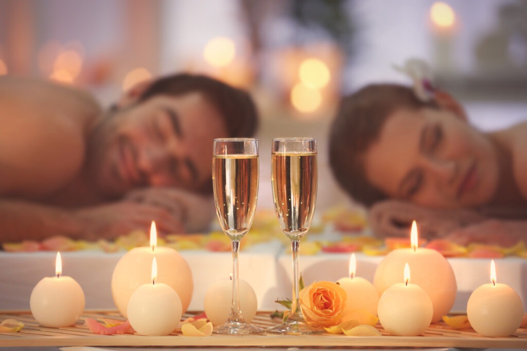 Paar entspannt bei einer romantischen Wellnessauszeit mit Kerzen, Rosenblüten und zwei Gläsern Sekt.