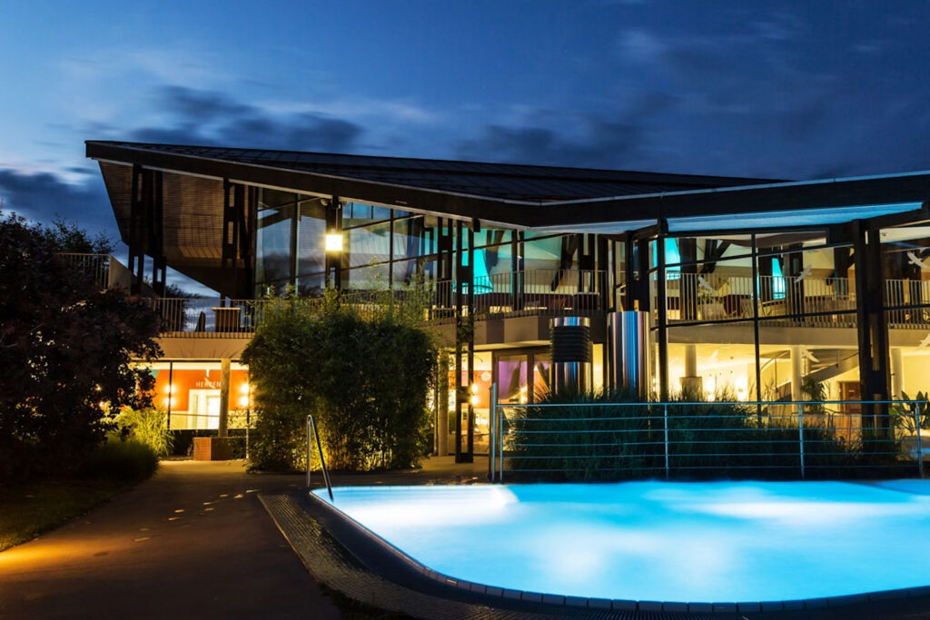 Zwei lächelnde Frauen liegen entspannt auf Handtüchern in einer Holzsauna im Warmbad Villach.