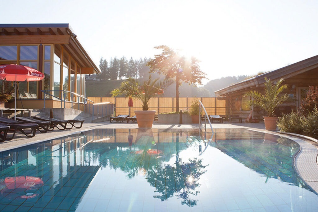 Zwei lächelnde Frauen liegen entspannt auf Handtüchern in einer Holzsauna im Warmbad Villach.