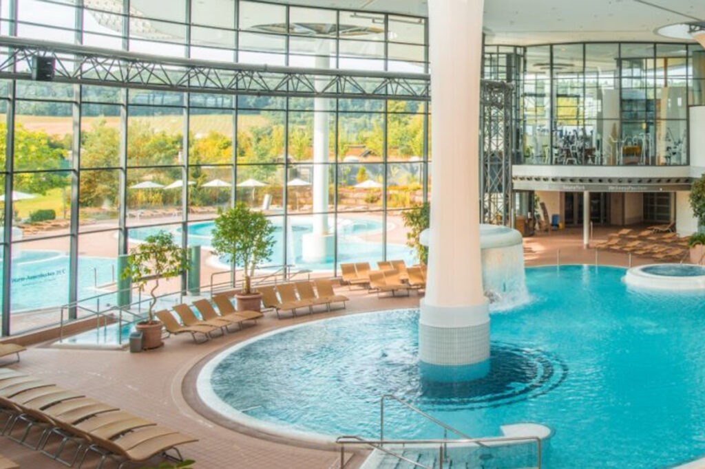 Zwei lächelnde Frauen liegen entspannt auf Handtüchern in einer Holzsauna im Warmbad Villach.