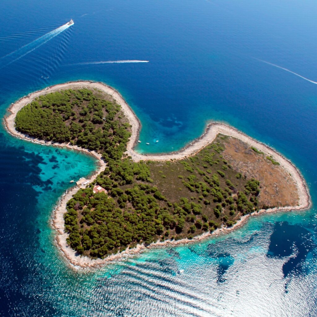FKK-Strand Jerolim – Pakleni Inseln, Hvar, Kroatien Luftaufnahme vom FKK-Strand Jerolim auf der Pakleni-Insel bei Hvar, umgeben von türkisblauem Meer und Pinienwäldern.