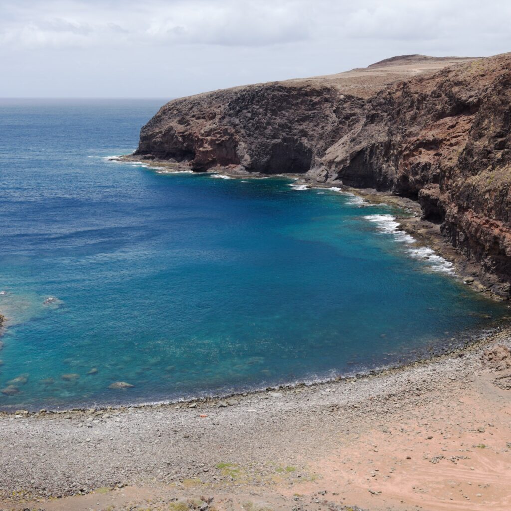 Kieselstrand und Steilküste an der Playa de Puerto de Las Nieves im Nordwesten von Gran Canaria mit klarem, türkisblauem Wasser.