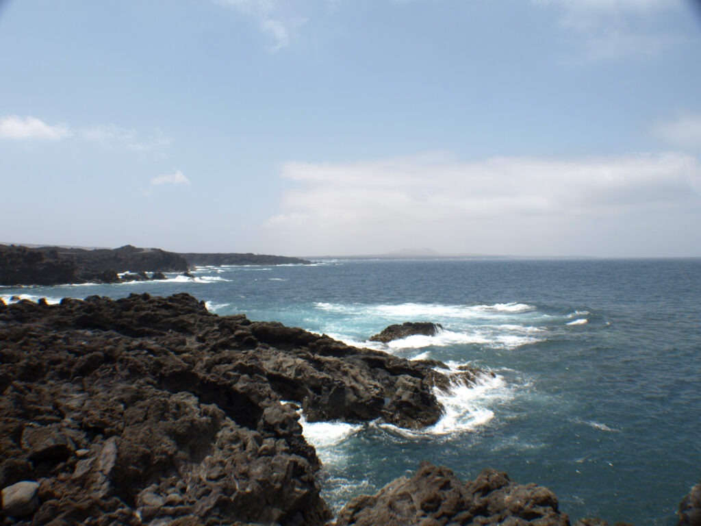 Felsen WestkĂŒste von Lanzarote Blick auf den FKK-Strand von Playa del InglĂ©s mit DĂŒnen, Palmen und weitem Meer.