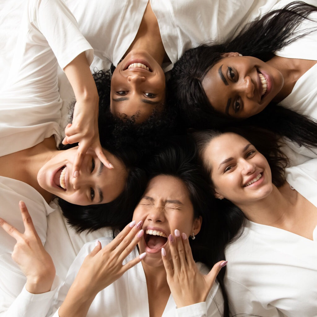 Five happy diverse young girls lying on bed, top view Zwei lächelnde Frauen liegen entspannt auf Handtüchern in einer Holzsauna im Warmbad Villach.