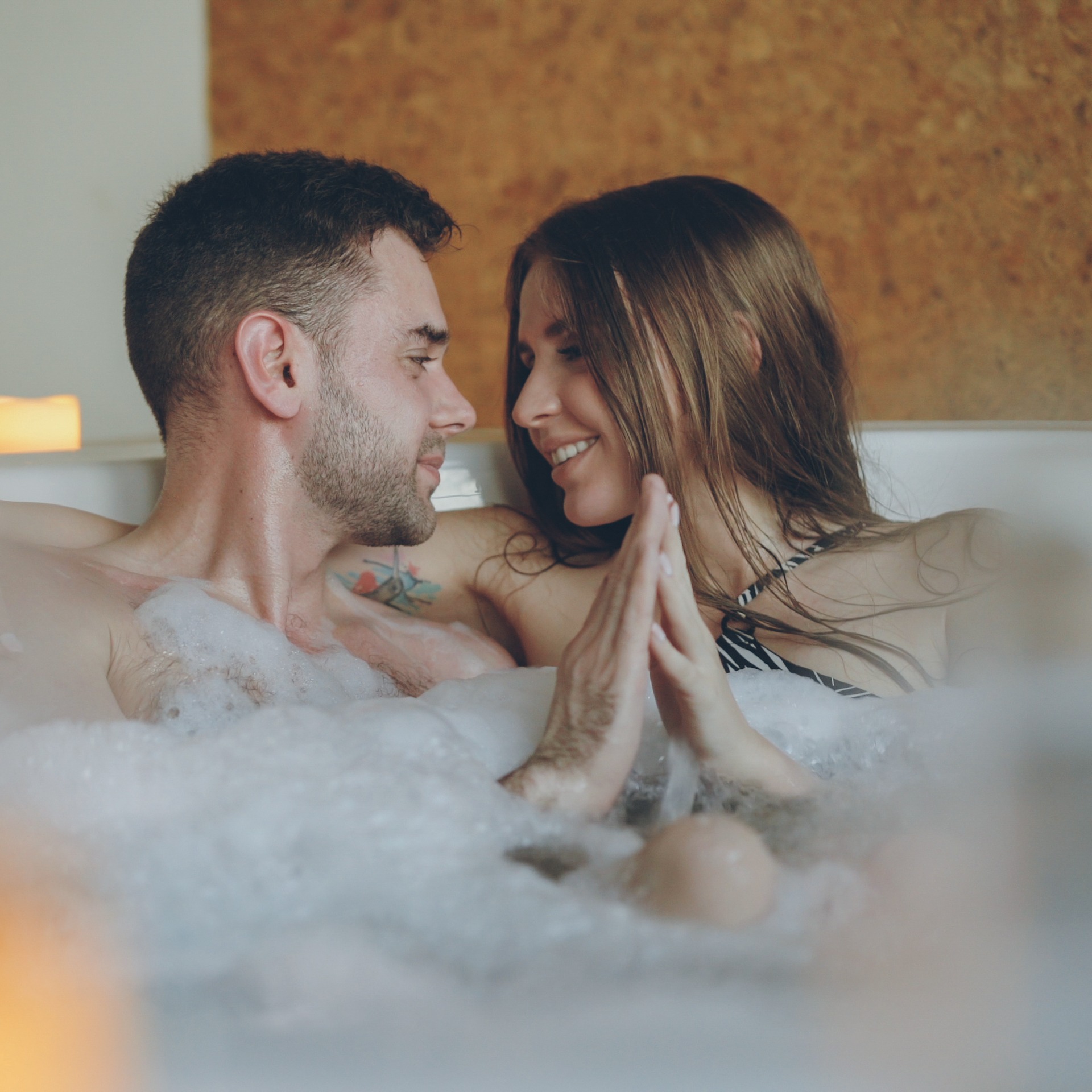 Newly married couple is relaxing in jacuzzi kissing, touching hands, talking and laughing. Romantic relationship, passionate honeymoon and wellness concept. Zwei lächelnde Frauen liegen entspannt auf Handtüchern in einer Holzsauna im Warmbad Villach.