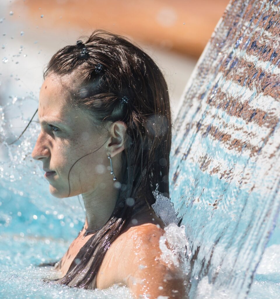 Junge Frau entspannt unter einem kraftvollen Wasserfall im Spa- oder Thermalbereich.