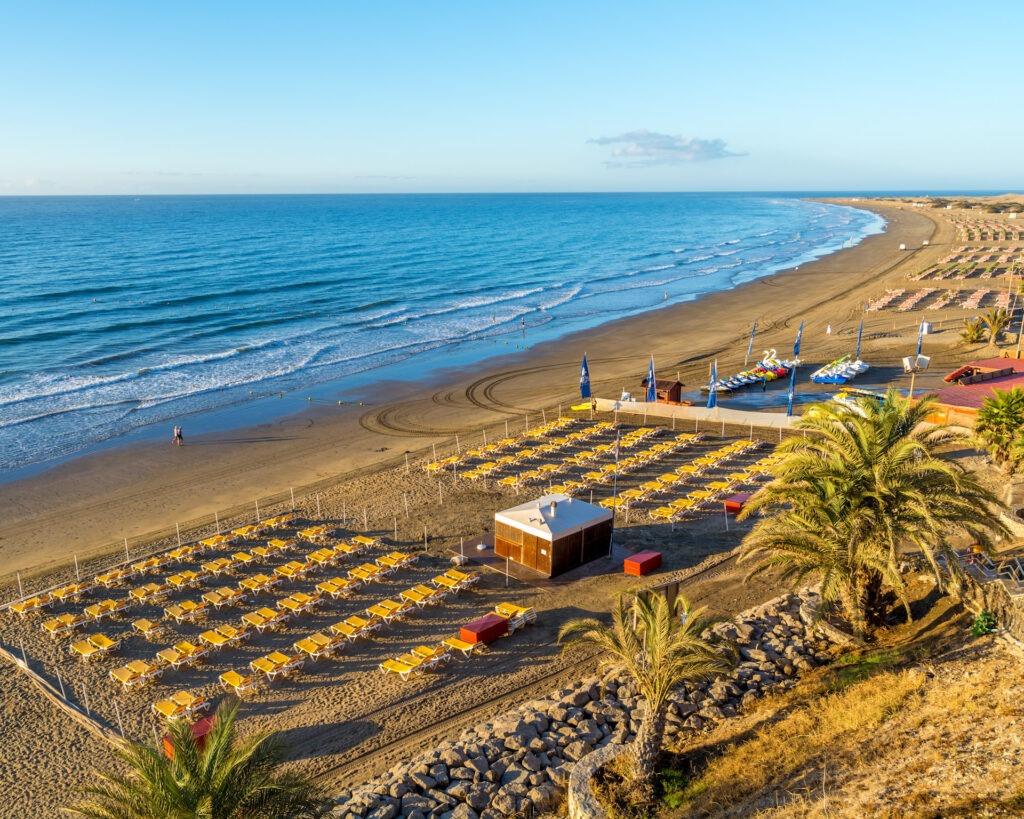 Blick auf den FKK-Strand von Playa del Inglés mit Dünen, Palmen und weitem Meer.