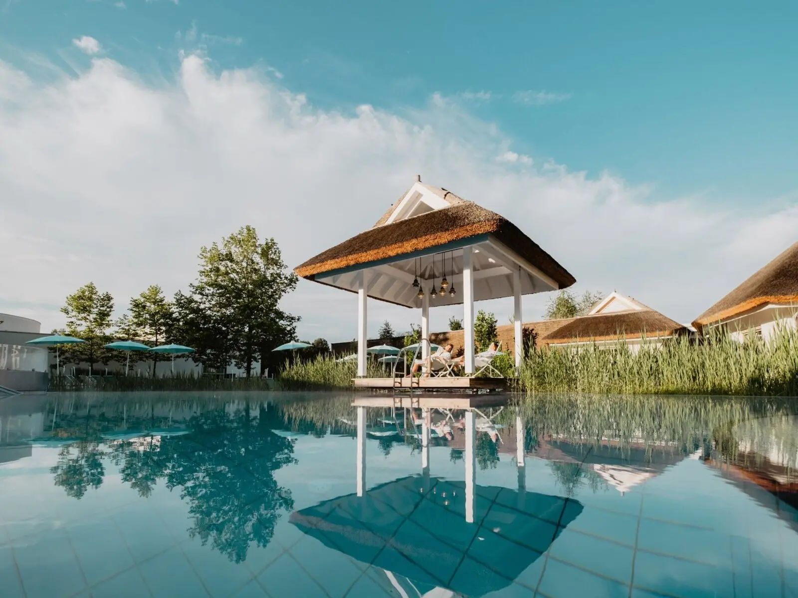 FKK-Resort Desire Riviera Maya mit Palmen, Gartenwegen und Strohdach-Pavillons in der Sonne.