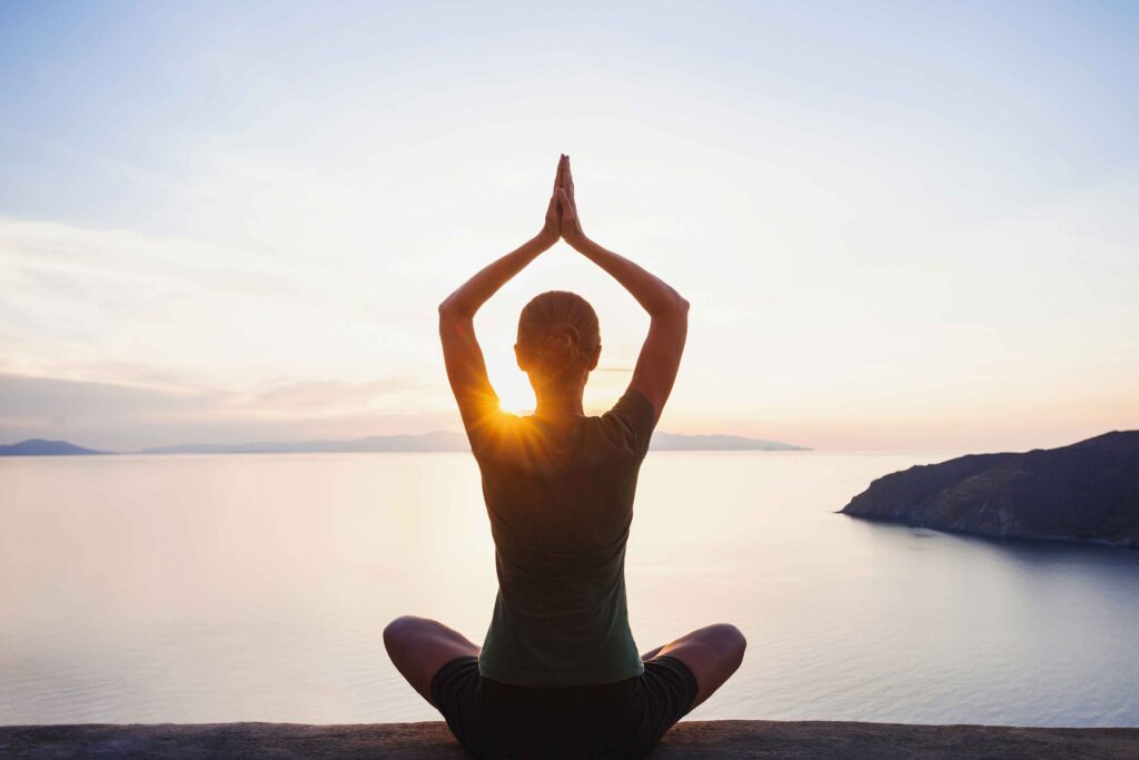 Frau beim Yoga am Meer bei Sonnenuntergang im Sizilien-Urlaub