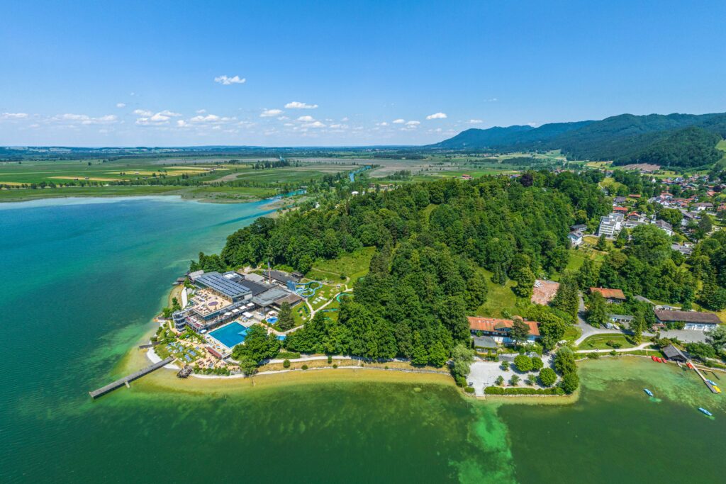 Ausblick auf den Kochelsee und die Gemeinde Kochel am See im Tölzer land Kristall Trimini Therme Kochel am See – Thermalbecken und Saunalandschaft mit Berg- und Seeblick, Ort für FKK-Wellness und Entspannung in Bayern.